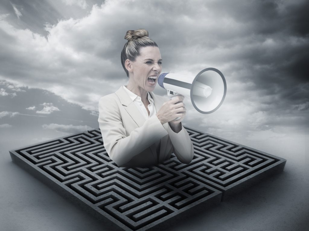 Annoyed businesswoman screaming in a megaphone above a maze in cloudy landscape
